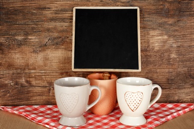 Photo of Ceramic cups on table near small chalkboard