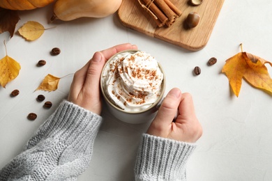 Photo of Woman with cup of tasty pumpkin spice latte at light table, above view