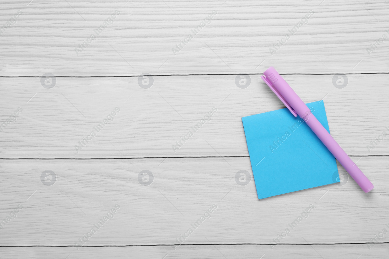 Photo of Paper note and purple marker on white wooden background, top view. Space for text
