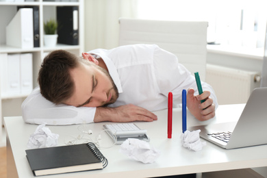 Photo of Lazy young man wasting time at messy table in office