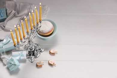 Hanukkah celebration. Menorah with burning candles, dreidels and gift boxes on white wooden table, above view. Space for text