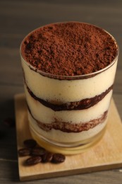 Photo of Delicious tiramisu in glass and coffee beans on wooden table, closeup