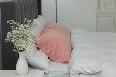 Photo of Vase with beautiful flowers on white bedside table and comfortable bed in room. Stylish interior