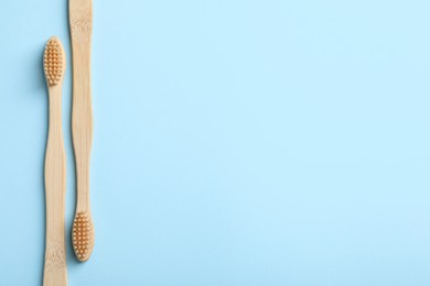 Two bamboo toothbrushes on light blue background, flat lay. Space for text