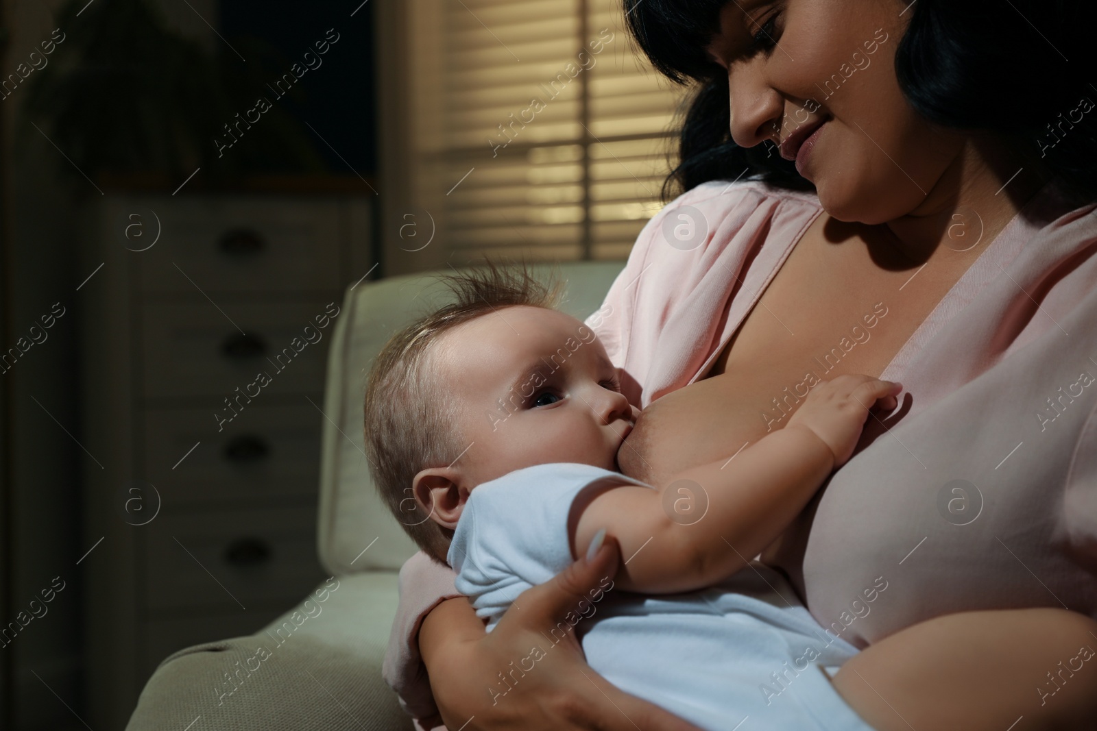 Photo of Woman breastfeeding her little baby on sofa in evening