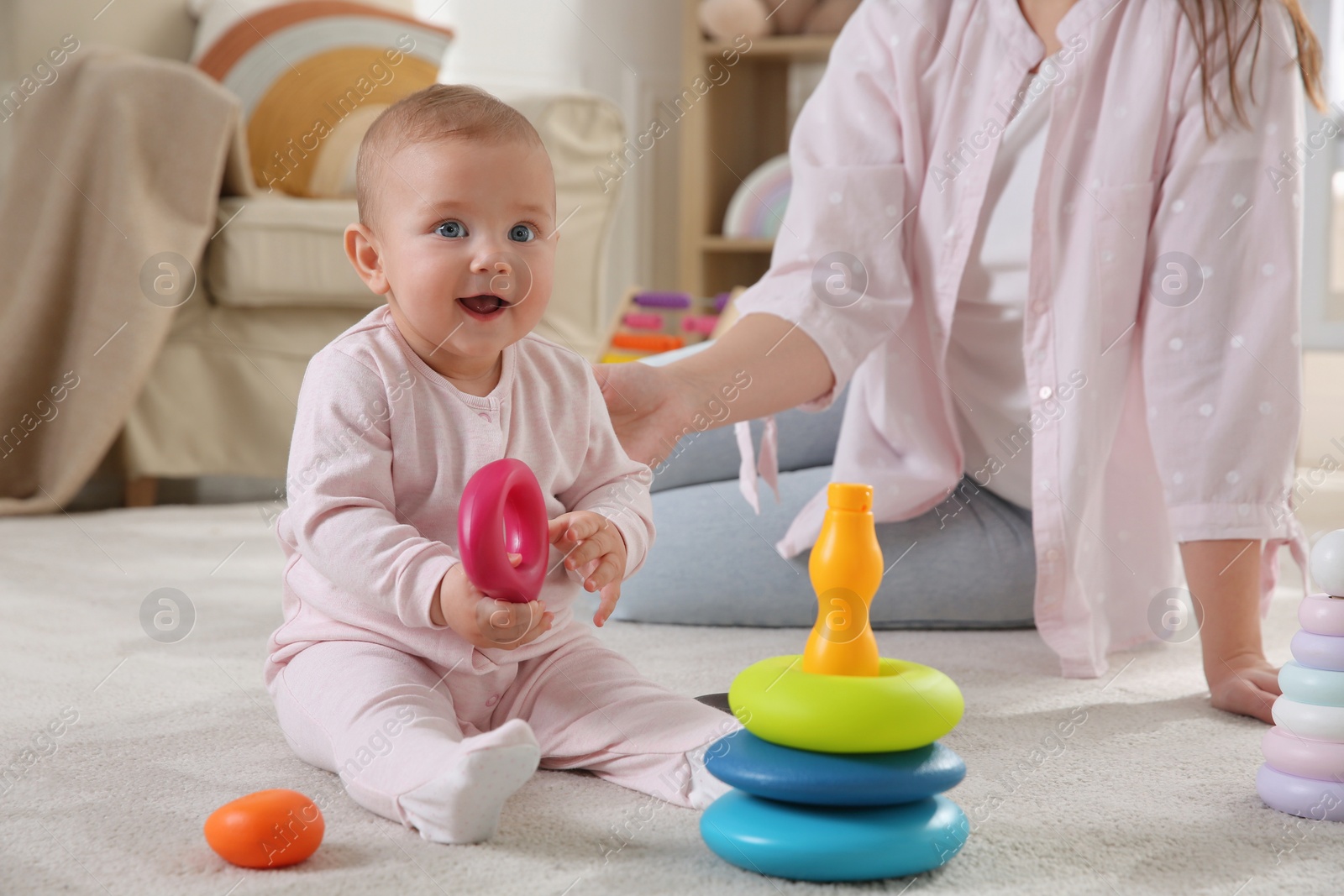 Photo of Cute baby girl and mother playing with toy pyramid on floor at home