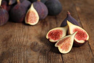 Whole and cut tasty fresh figs on wooden table, space for text
