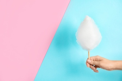 Photo of Woman holding stick with fluffy cotton candy on color background, closeup. Space for text