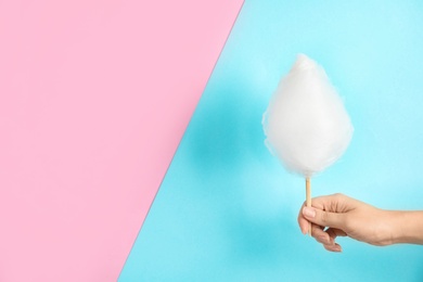 Woman holding stick with fluffy cotton candy on color background, closeup. Space for text