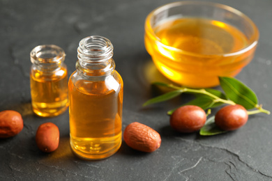 Jojoba oil and seeds on dark grey table