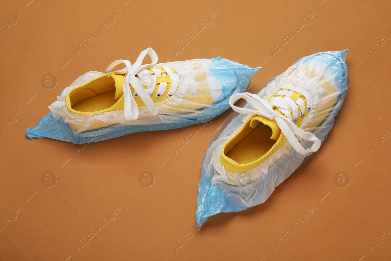 Photo of Sneakers in shoe covers on brown background, above view