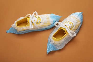 Photo of Sneakers in shoe covers on brown background, above view