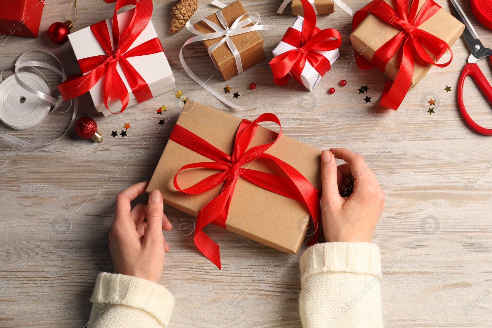 Photo of Woman decorating gift box at white wooden table, top view. Christmas present