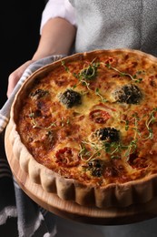 Photo of Woman holding delicious homemade vegetable quiche on black background, closeup