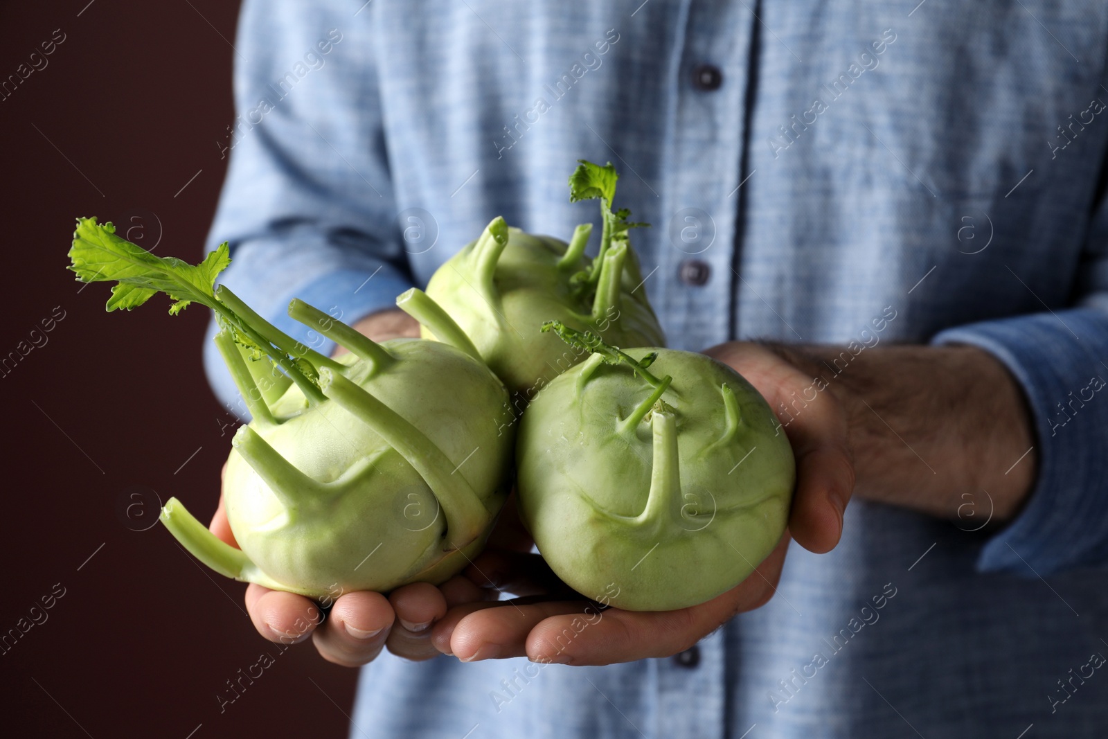 Photo of Man with ripe kohlrabi plants on brown background, closeup