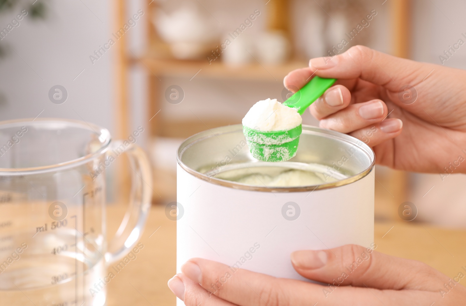 Photo of Woman preparing infant formula at table indoors, closeup. Baby milk