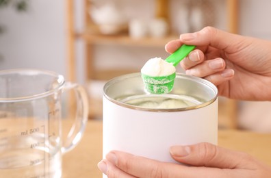 Photo of Woman preparing infant formula at table indoors, closeup. Baby milk