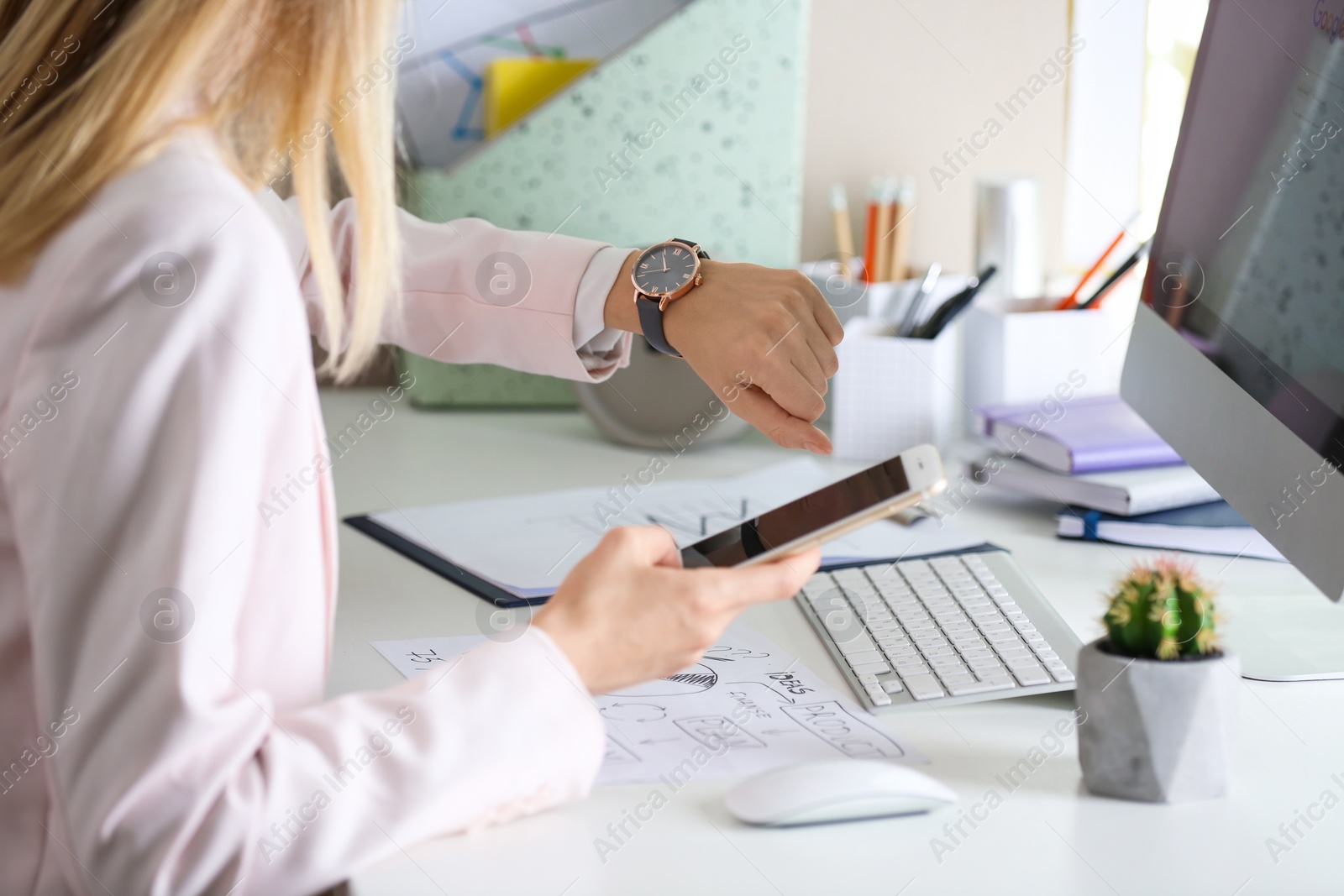 Photo of Young woman checking time on her wristwatch at workplace