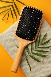 Photo of Wooden hairbrush, towel and green leaves on orange background, flat lay