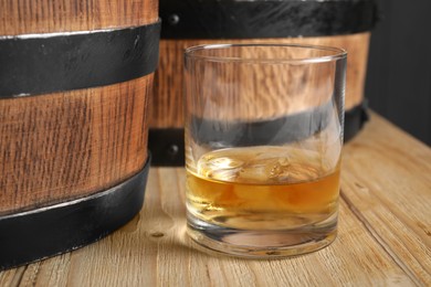Photo of Barrels and glass of tasty whiskey on wooden table, closeup