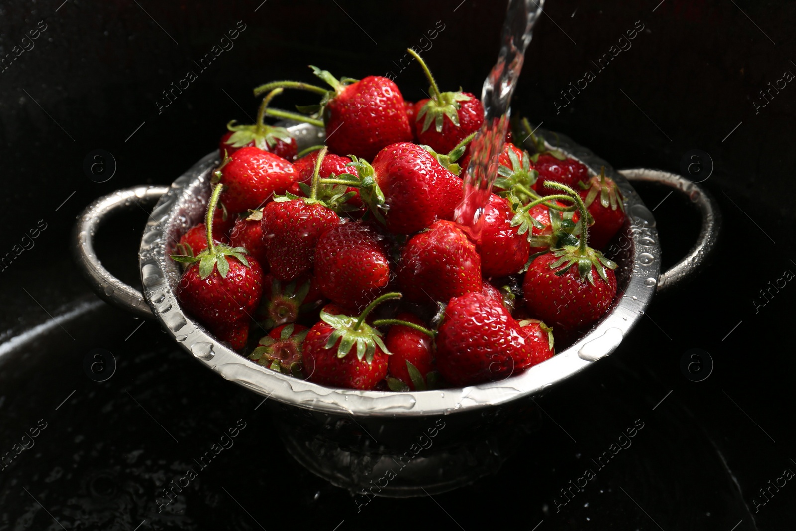 Photo of Washing fresh strawberries under tap water in metal colander in sink