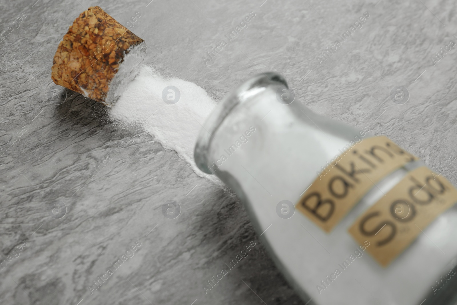 Photo of Overturned glass bottle with baking soda on grey table, closeup