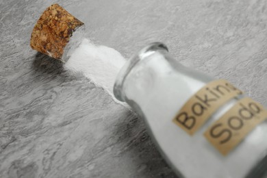 Photo of Overturned glass bottle with baking soda on grey table, closeup