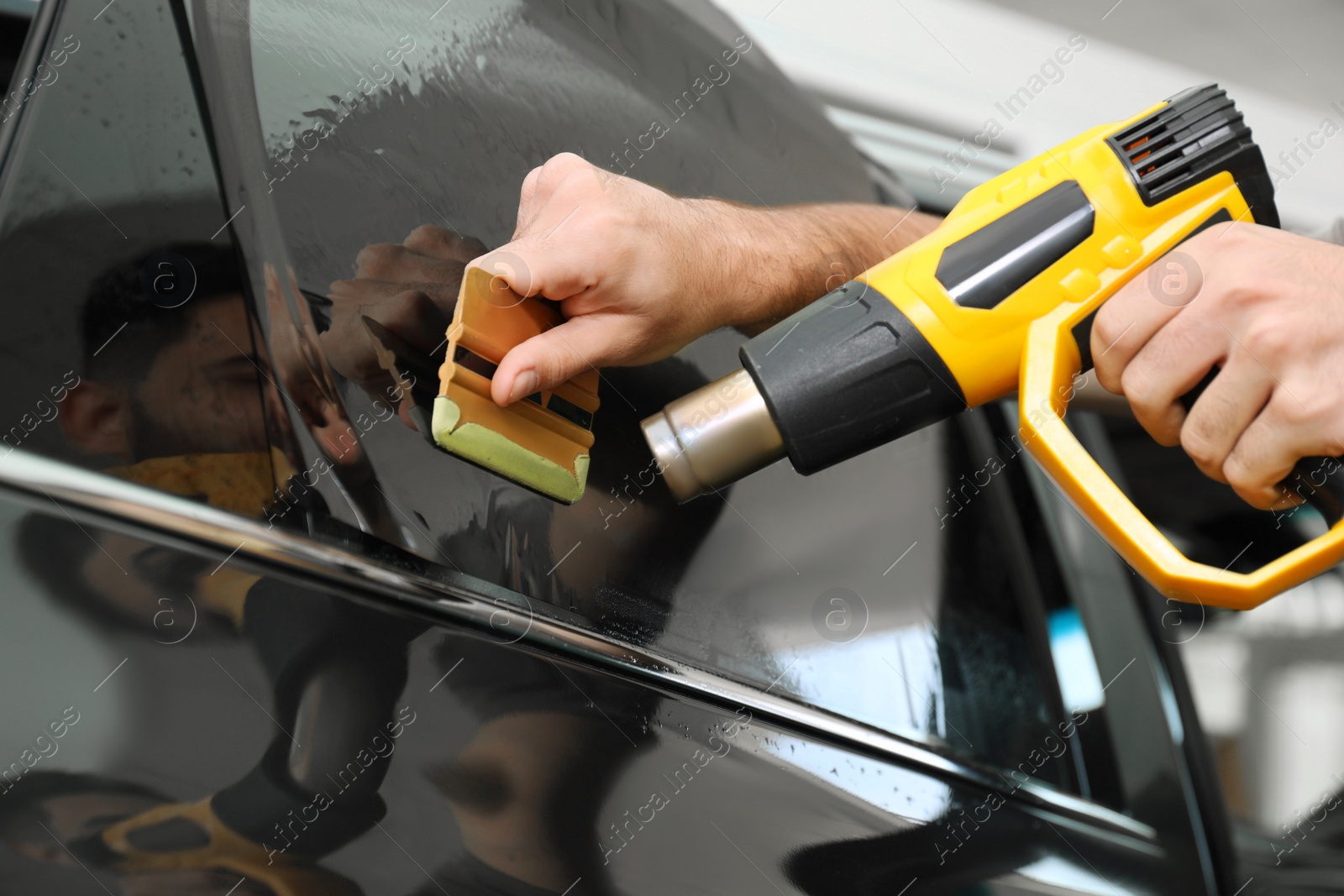 Photo of Worker tinting car window with heat gun in workshop, closeup