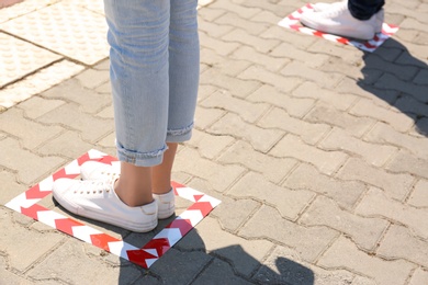 People standing on taped floor markings for social distance outdoors, closeup. Coronavirus pandemic