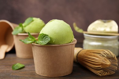 Photo of Paper cups with tasty matcha ice cream and bamboo whisk on wooden table, closeup