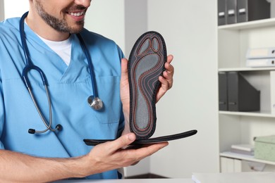 Male orthopedist showing insoles in hospital, closeup