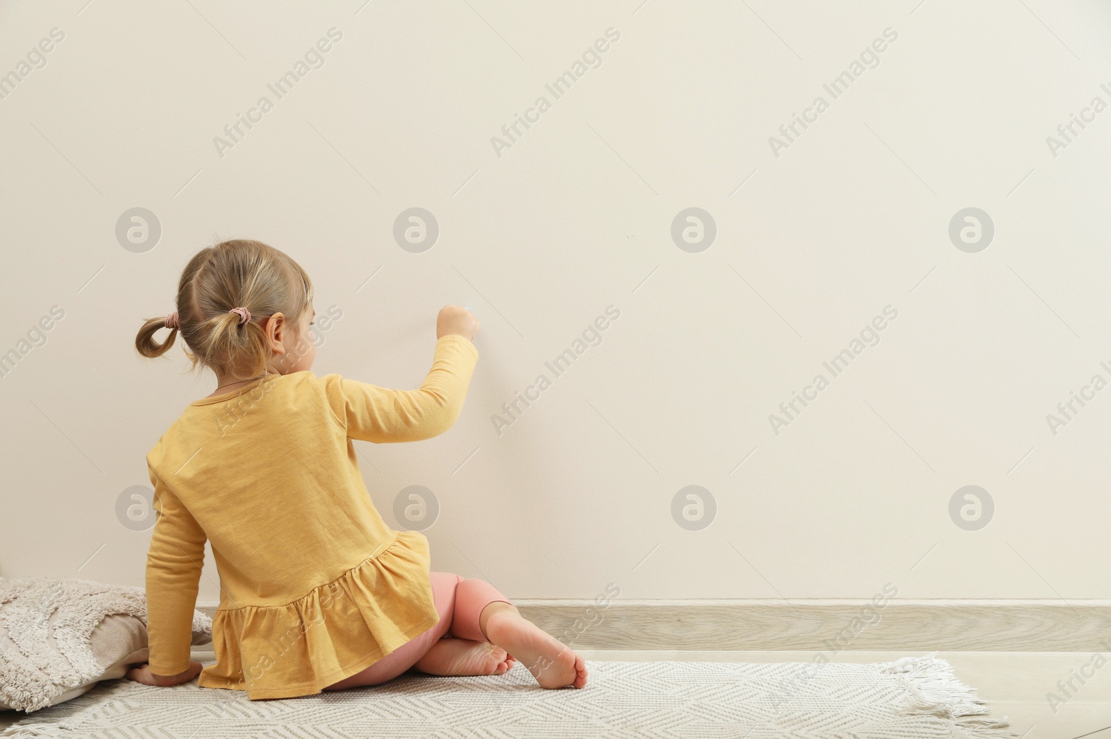 Photo of Little girl drawing on beige wall indoors, back view and space for text. Child`s art