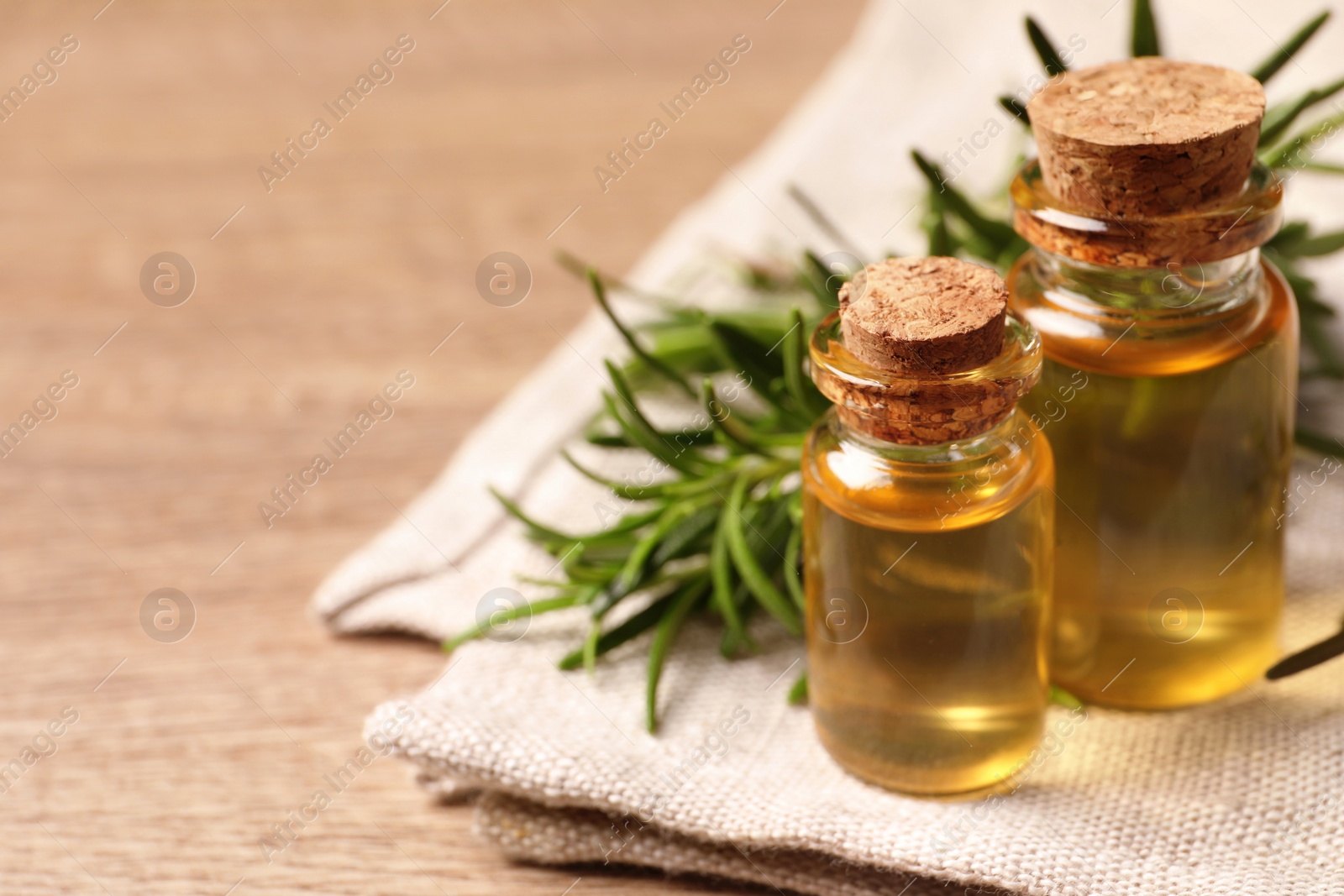 Photo of Bottles with oil and fresh rosemary on wooden table, space for text