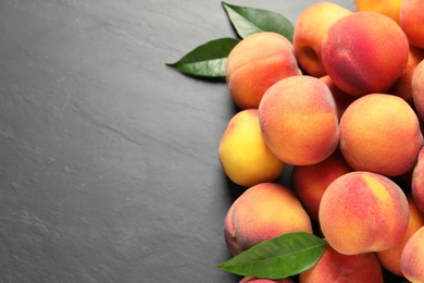 Fresh peaches and leaves on dark grey textured table, flat lay. Space for text