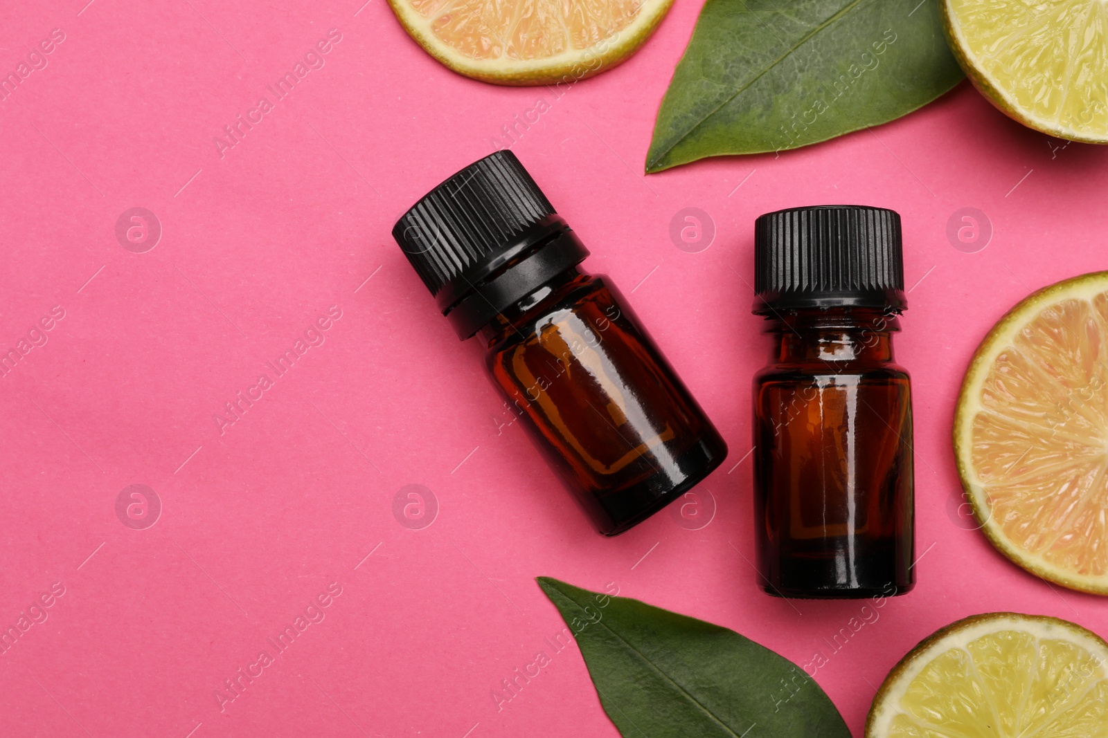 Photo of Bottles of citrus essential oil and fresh lime slices on pink background, flat lay. Space for text