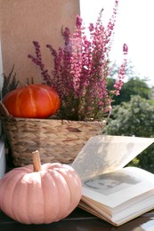 Wicker basket with beautiful heather flowers, pumpkins and open book on windowsill outdoors