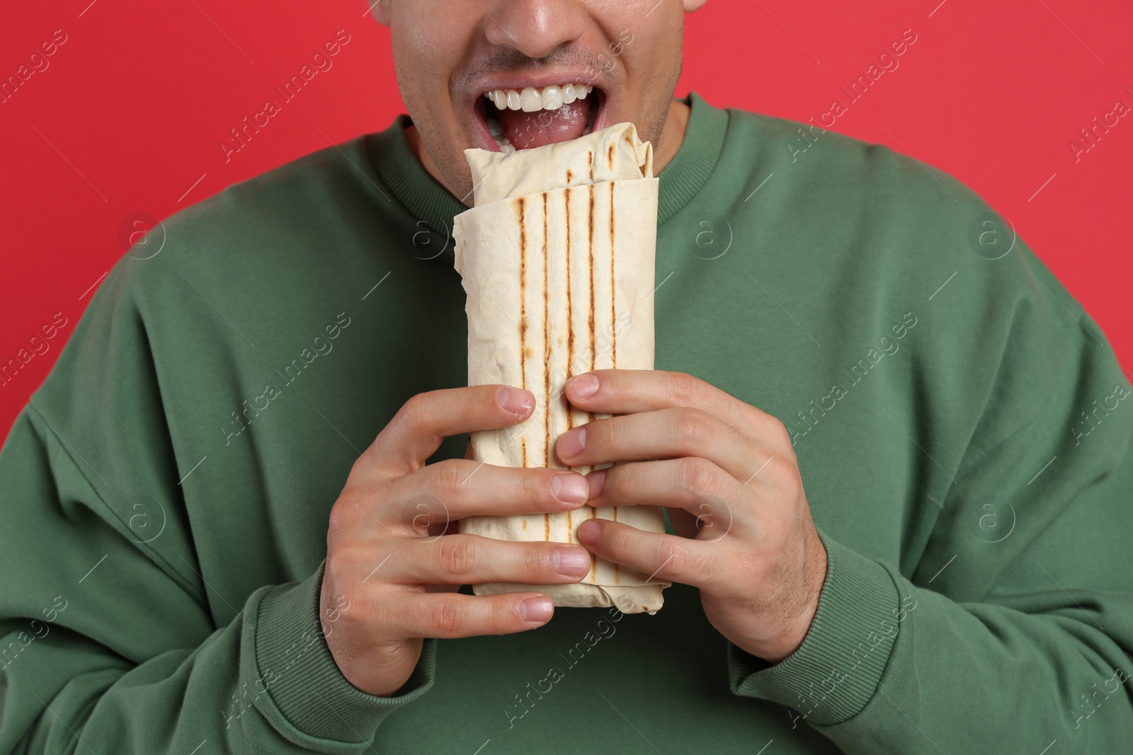 Photo of Man eating delicious shawarma on red background, closeup