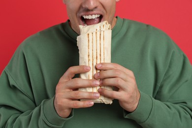 Photo of Man eating delicious shawarma on red background, closeup