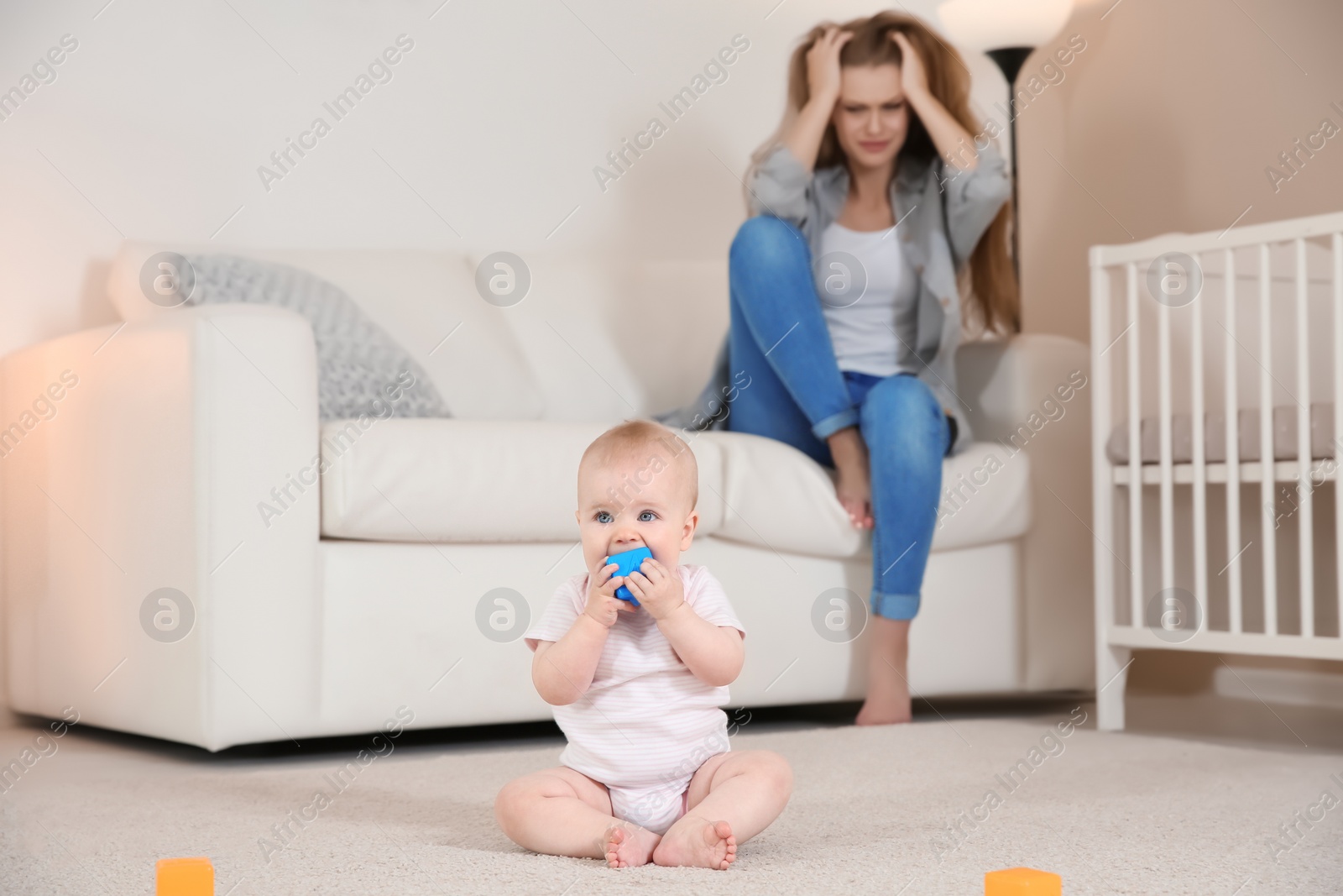 Photo of Cute baby girl playing on floor and young mother suffering from postnatal depression at home