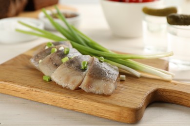 Wooden board with delicious salted herring slices and green onion on white table, closeup
