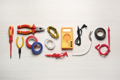 Photo of Different wires and electrician's tools on white wooden table, flat lay