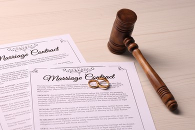 Marriage contracts, gold rings and gavel on light wooden table, closeup