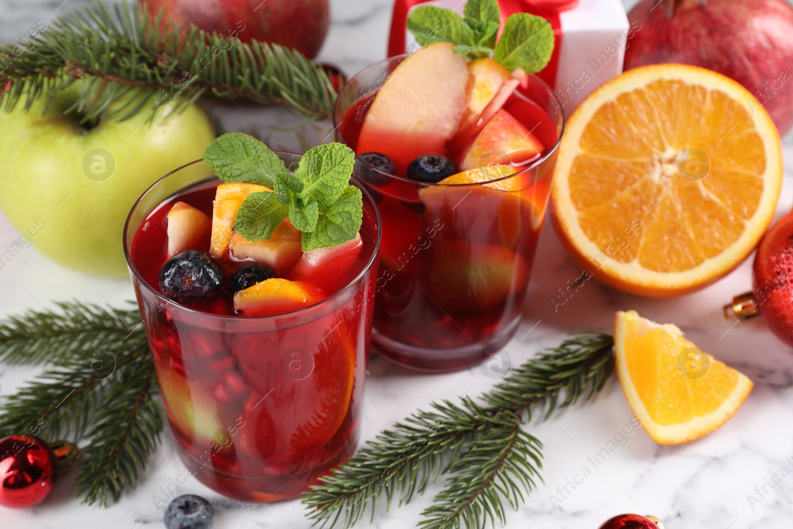 Photo of Aromatic Sangria drink in glasses, ingredients and Christmas decor on white marble table