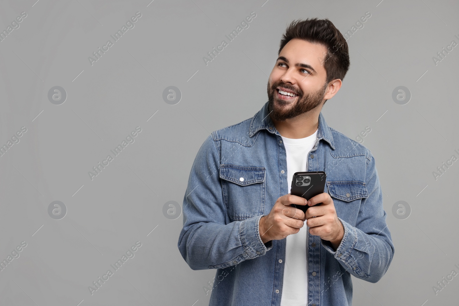 Photo of Happy young man using smartphone on grey background, space for text