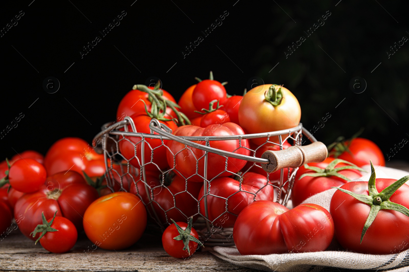 Photo of Many different ripe tomatoes on wooden table against dark background