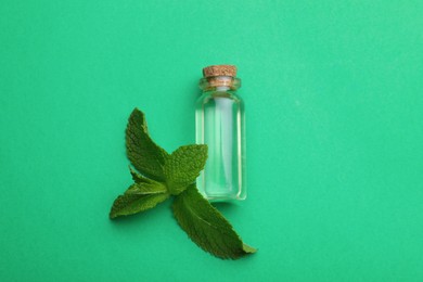 Photo of Bottle of essential oil and mint on green background, flat lay