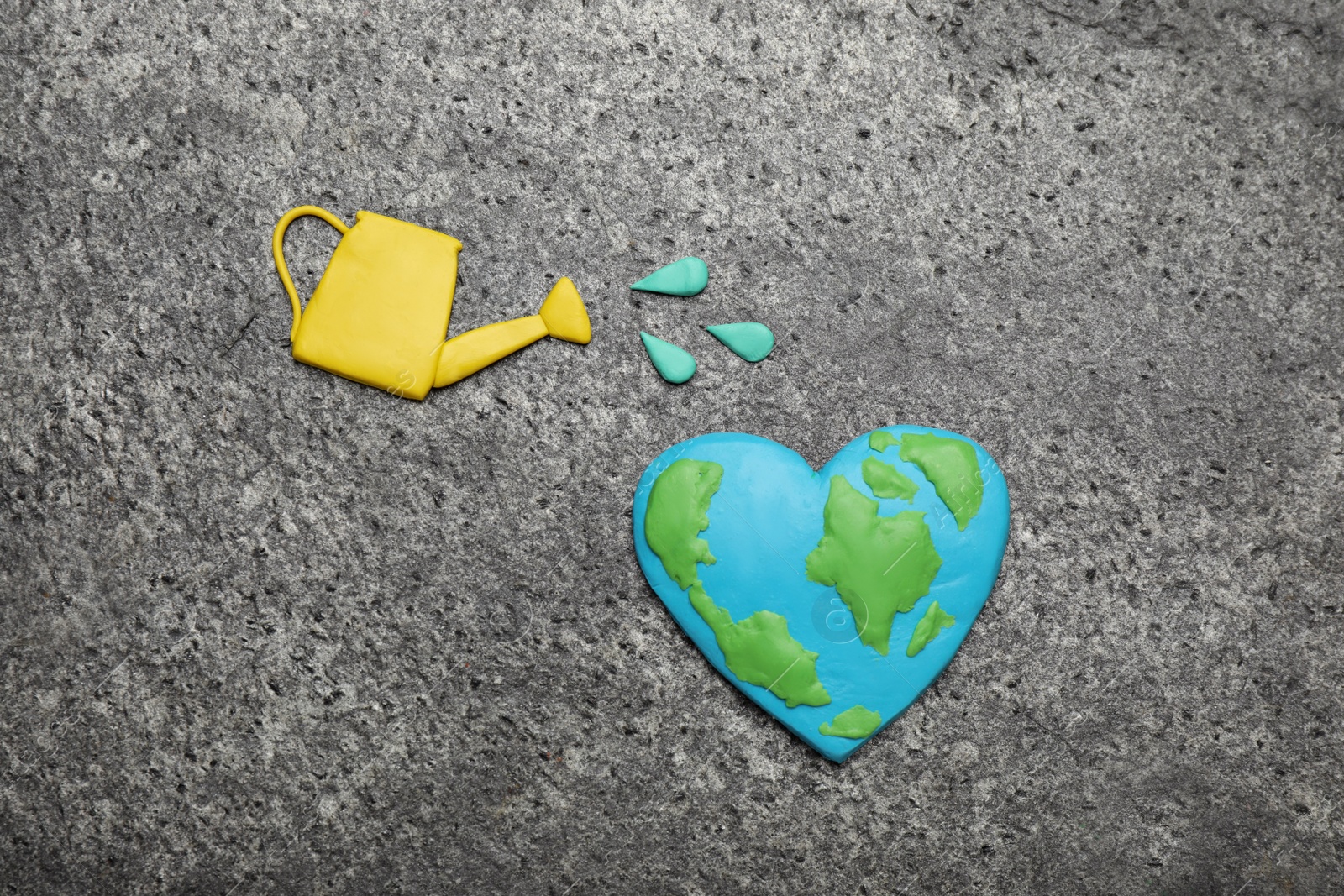 Photo of Happy Earth Day. Flat lay composition with plasticine planet and watering can on grey table