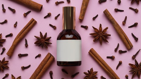 Flat lay composition with bottle of perfume surrounded by cloves and cinnamon sticks on pink background