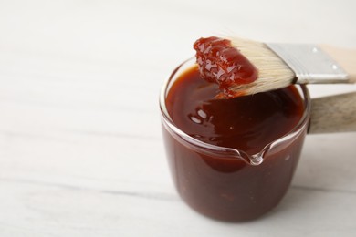 Photo of Marinade and basting brush on white table, closeup. Space for text