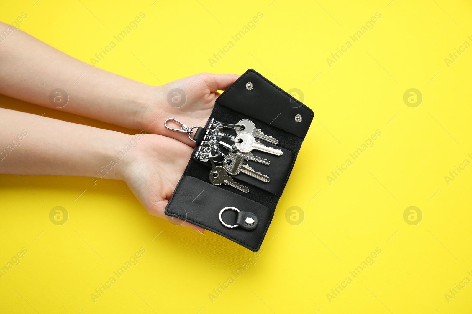 Photo of Woman holding open leather holder with keys on yellow background, top view